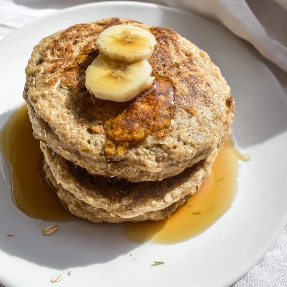 Golden-brown banana oat pancakes, stacked high, ready to be enjoyed with fresh sliced fruit.