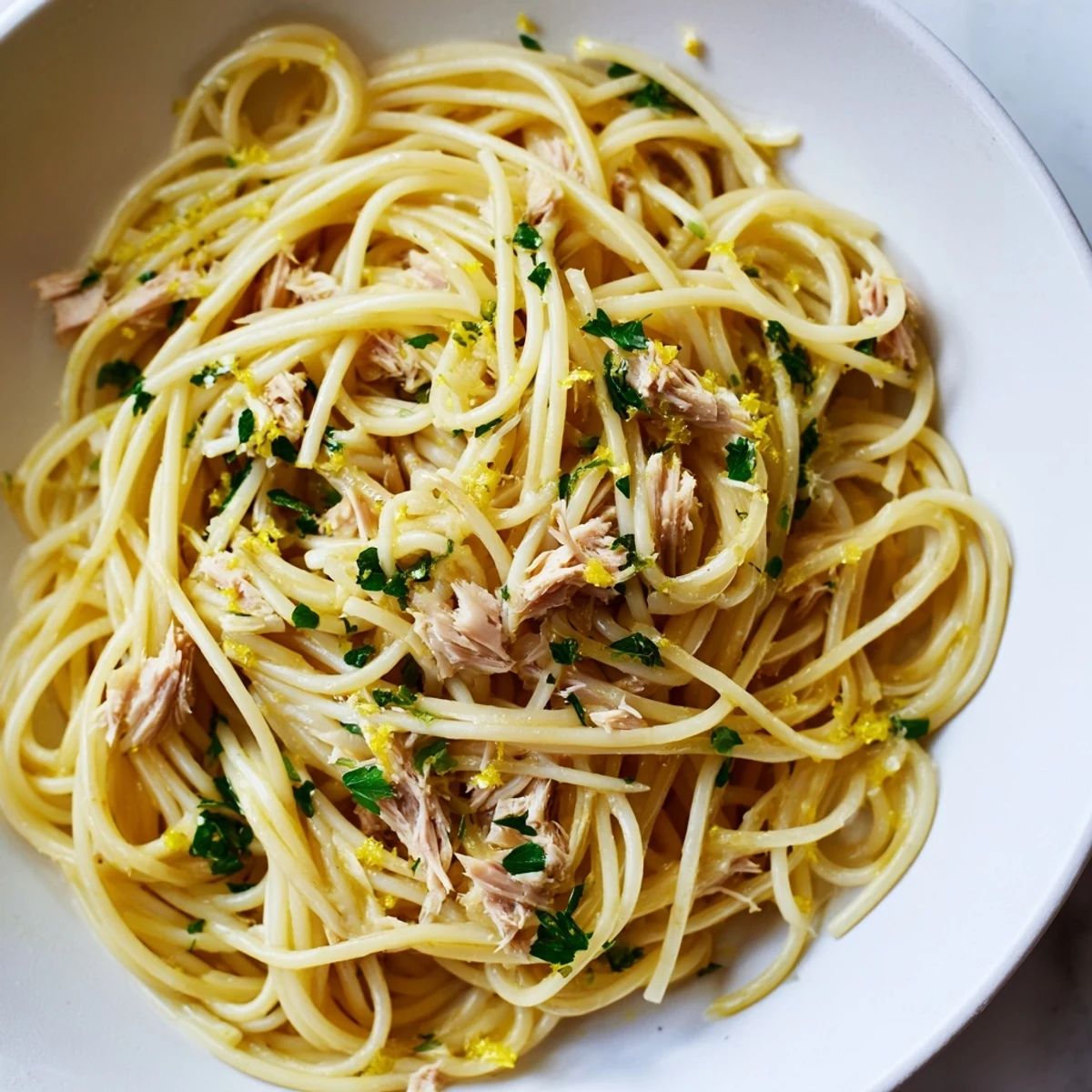 Freshly made Lemon-Garlic Tuna Spaghetti, ready to serve, garnished with parsley and lemon wedges.