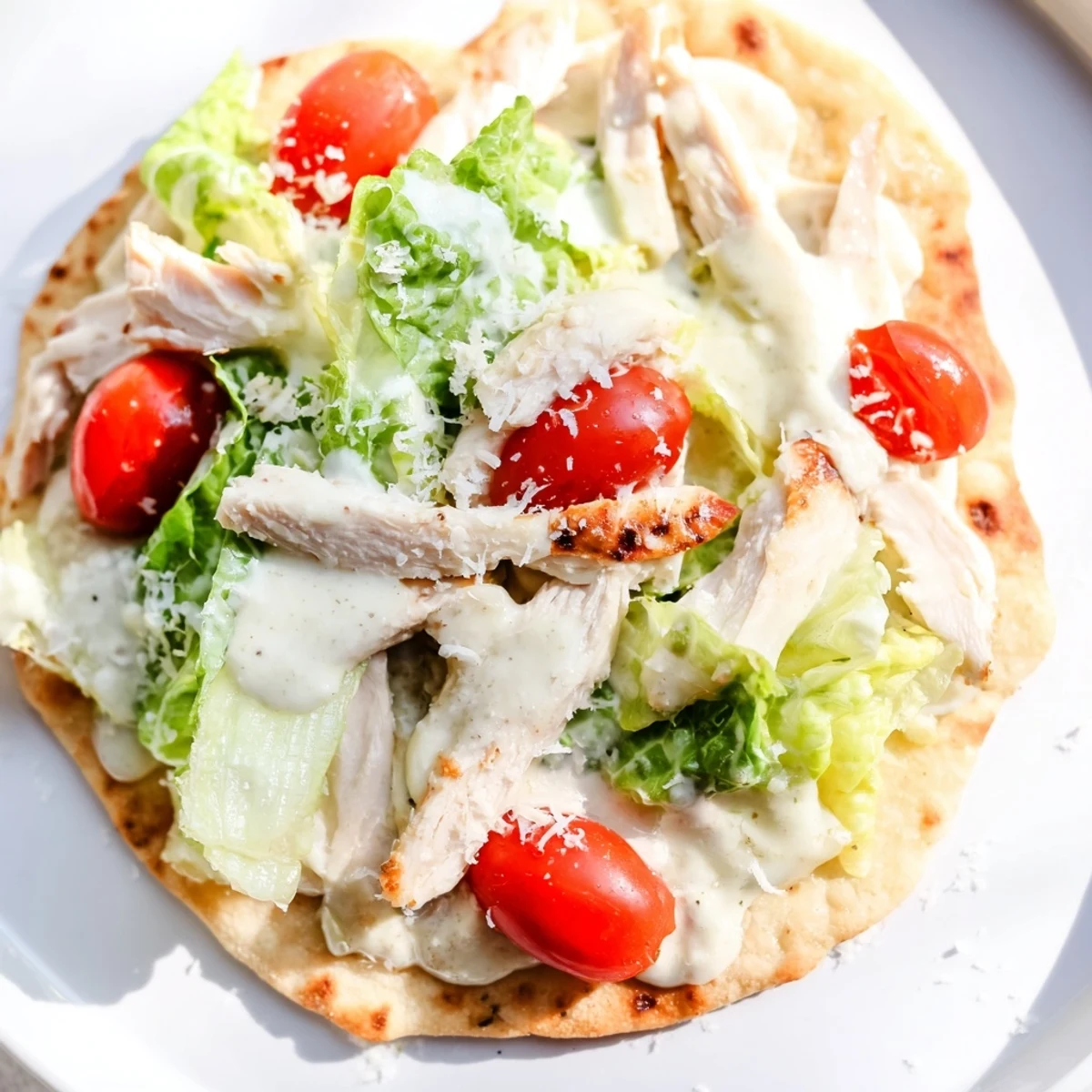 Sizzling grilled chicken layered over warm flatbread with Caesar salad and cherry tomatoes, ready to serve.
