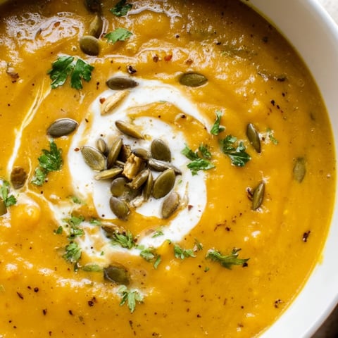 Geröstete Kürbissuppe mit Kokoscreme, würzigen Aromen und frischen Kürbiskernen serviert.  