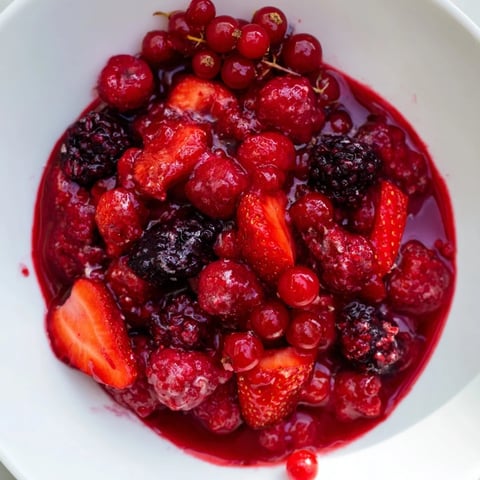 A vibrant bowl of Rote Grütze with a generous pour of creamy vanilla sauce, ready to serve.