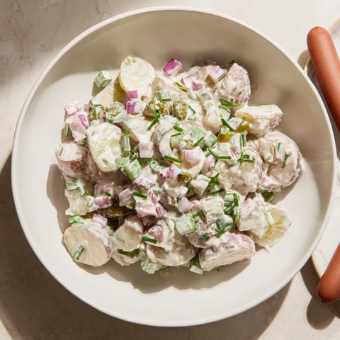 Savory German potato salad with sizzling sausages, a hearty meal served warm.