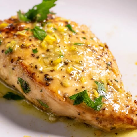 Goldene Hähnchenbruststücke in einer glänzenden Zitronen-Pfeffer-Buttersauce auf einem Teller garniert mit frischem Petersilie.