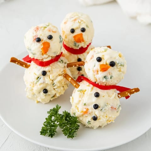 Three festive Snowman Cheese Ball Trio appetizers, ready to be enjoyed with crackers and fresh vegetables.