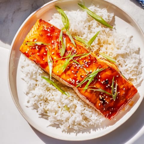 Pan-seared sticky orange salmon showing juicy flakes, paired with hot rice and green scallions.
