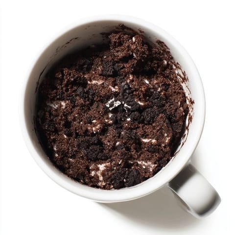 Steaming-hot Oreo mug cake topped with a dollop of whipped cream, ready for a sweet treat.