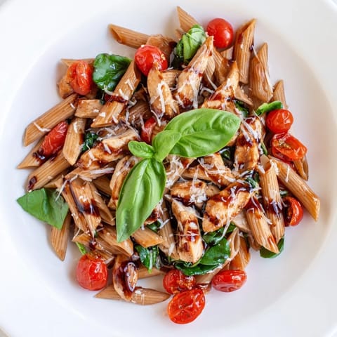 Frisch zubereitetes Balsamic Glazed Chicken Pasta mit glasiertem Hähnchen und Babyspinat auf einem weißen Teller.