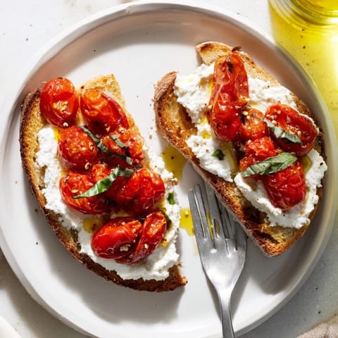 Heiße, geröstete Cherrytomaten auf knusprigem Sauerteigbrot mit cremiger Ricotta-Creme und frischen Basilikumblättern garniert.