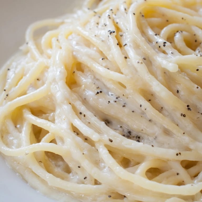 Depicts freshly cracked black pepper sprinkled over hot Spaghetti Cacio e Pepe, paired with a crisp glass of white wine.