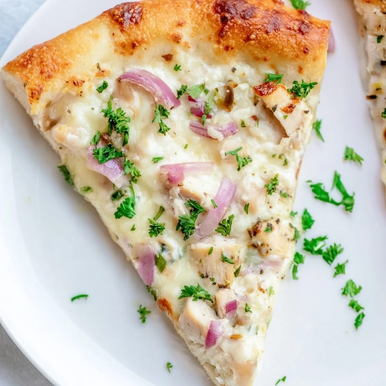 Close-up of Chicken Alfredo Pizza topped with fresh parsley and grated Parmesan, served hot on a counter.