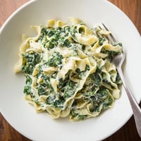 Cremige Spinat-Knoblauch-Nudeln in einer reichhaltigen Sahnesauce, garniert mit frischem Parmesan und roten Pfefferflocken auf einem Holztisch.