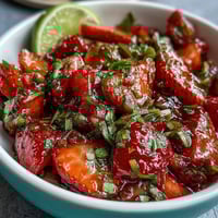 Frische Erdbeer-Salsa mit Limette und Jalapeño auf einem weißen Teller, mit bunten Früchten und grünen Kräutern.  