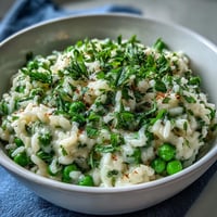 Frischer, cremiger Erbsen-Minze-Risotto mit Parmesan, garniert mit Minzblättern und Zitronenzesten.